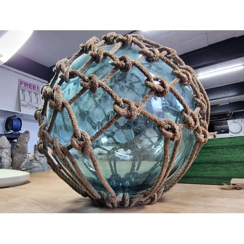 94 - Antique glass hand blown fishing float buoy in good order with original netting surround, the buoy m... 