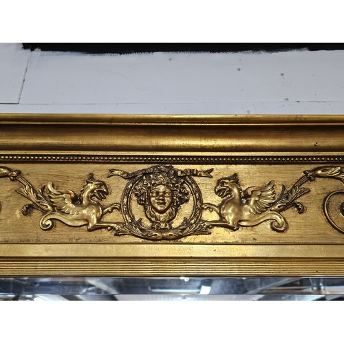 54 - A large ornate gilded triple over mantle bevel edged mirror with a Egyptian frieze to the top, a pha... 