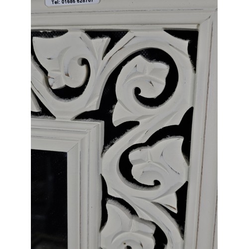 207 - An ornate wooden mirror with intricate scroll work and carved detailing to the border, in white wood... 