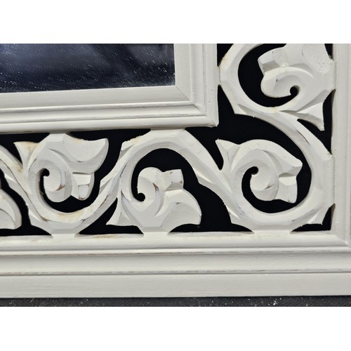 207 - An ornate wooden mirror with intricate scroll work and carved detailing to the border, in white wood... 