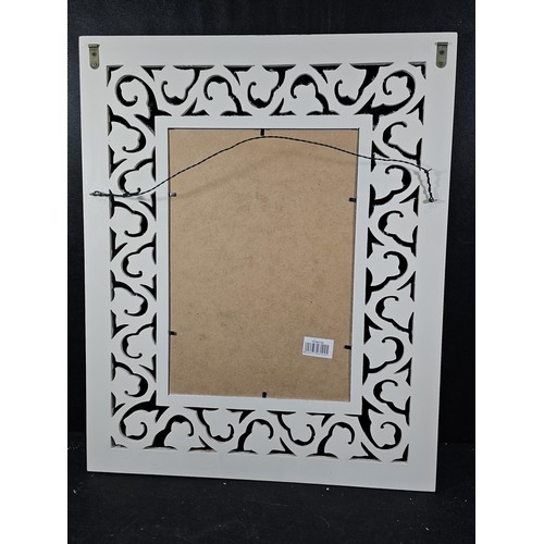 207 - An ornate wooden mirror with intricate scroll work and carved detailing to the border, in white wood... 
