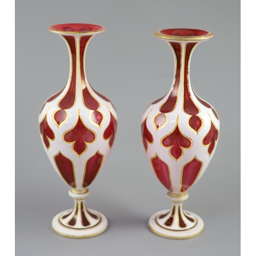 103 - A pair of Bohemian white and ruby overlaid glass vases, the shaped panel cuts with gilded edges, the... 