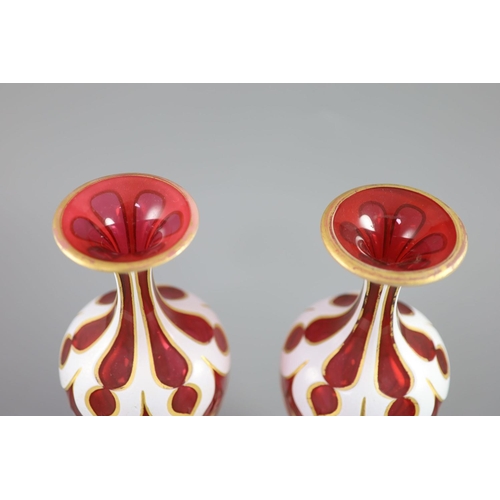 103 - A pair of Bohemian white and ruby overlaid glass vases, the shaped panel cuts with gilded edges, the... 