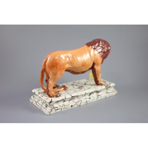 72 - An Enoch Wood pearlware figure of a Medici Lion, c.1800-10, with paw on a golden ball, on a marbled ... 