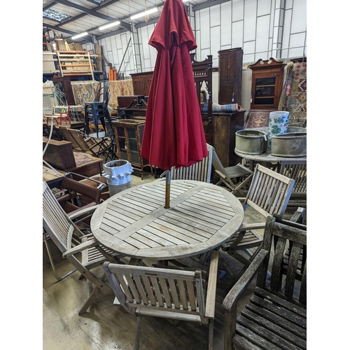 1067 - A circular weathered teak folding garden table, diameter 120cm, height 74cm, four folding elbow chai... 