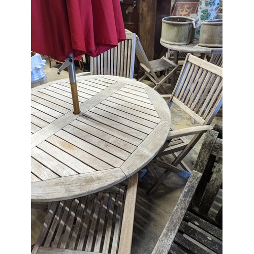 1067 - A circular weathered teak folding garden table, diameter 120cm, height 74cm, four folding elbow chai... 