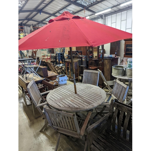 1067 - A circular weathered teak folding garden table, diameter 120cm, height 74cm, four folding elbow chai... 