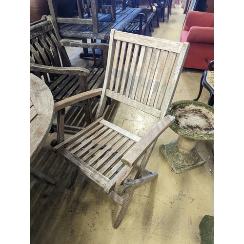 1067 - A circular weathered teak folding garden table, diameter 120cm, height 74cm, four folding elbow chai... 