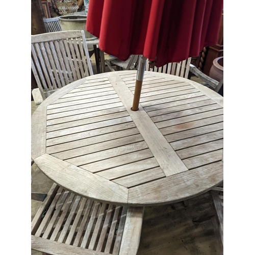 1067 - A circular weathered teak folding garden table, diameter 120cm, height 74cm, four folding elbow chai... 