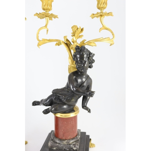 72 - A pair of Louis XVI style bronze and ormolu two light candelabra, each with seated putto stem and sc... 