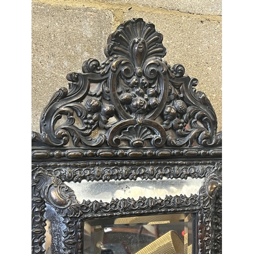 19 - A Dutch brass framed cushion wall mirror, with ornate arched cresting, pierced and repousse with bir... 