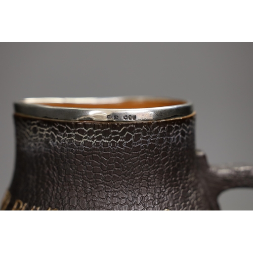 1329 - A Doulton Lambert black jug, 'He Who Buys Good Ale Buys Nothing Else', with silver mount, 19cm tall... 