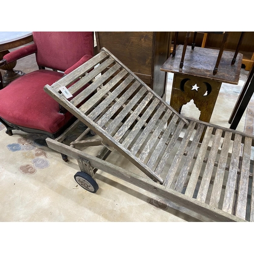 1057 - A weathered teak garden lounger on wheels, length 198cm