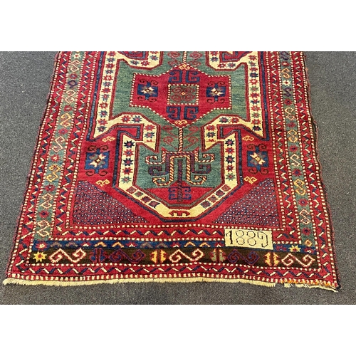 196 - An antique Kazak red ground rug, with double shield motif within a hooked geometric field and triple... 