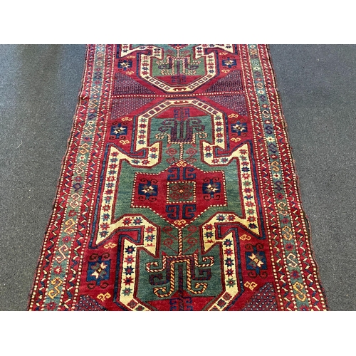 196 - An antique Kazak red ground rug, with double shield motif within a hooked geometric field and triple... 