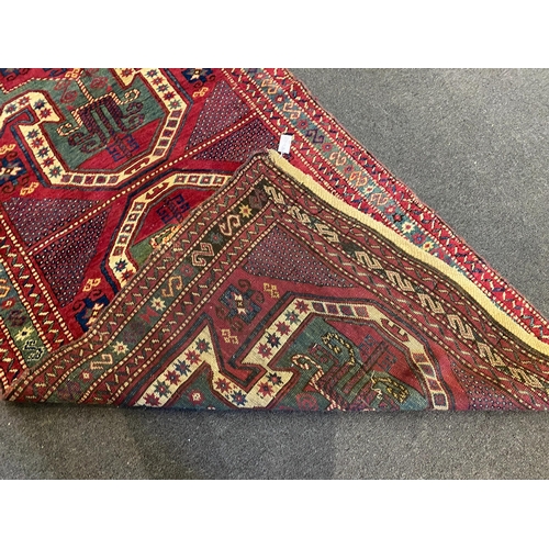 196 - An antique Kazak red ground rug, with double shield motif within a hooked geometric field and triple... 