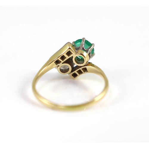 434 - A gold, emerald and diamond set two stone cross-over ring, with diamond set shoulders, the diamond a... 