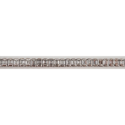 436 - A modern 18ct white gold and emerald cut diamond set line bracelet, the sixty nine stones with a tot... 