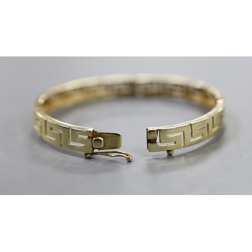 938 - A modern yellow metal hinged bangle with Greek Key decoration and a 9ct donkey and cart charm, gross... 