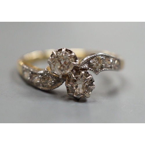 1932 - A yellow metal and two stone diamond set crossover ring, with diamond set shoulders, size J, gross w... 