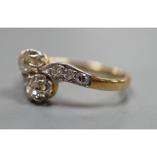 1932 - A yellow metal and two stone diamond set crossover ring, with diamond set shoulders, size J, gross w... 