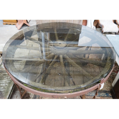 1106 - A wrought iron glass topped circular cartwheel garden table, diameter 124cm, height 72cm