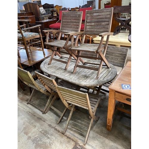 1175 - A weathered teak folding oval garden table, length 150cm, depth 91cm, height 74cm together with eigh... 