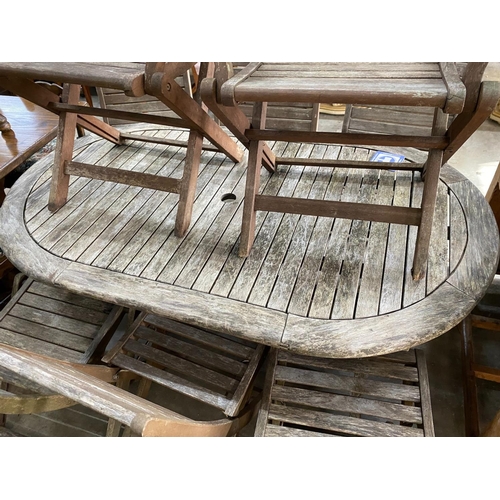 1175 - A weathered teak folding oval garden table, length 150cm, depth 91cm, height 74cm together with eigh... 