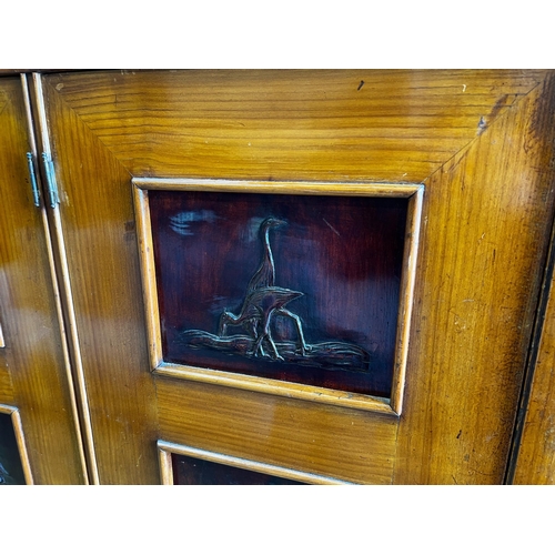 141 - A mid century continental side cabinet, the panelled doors carved with antelope and exotic birds, wi... 