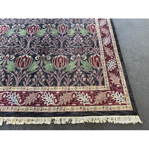 224 - A large Indian Arts & Crafts style carpet, with stylised pomegranate and flower motifs on a charcoal... 