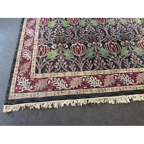 224 - A large Indian Arts & Crafts style carpet, with stylised pomegranate and flower motifs on a charcoal... 