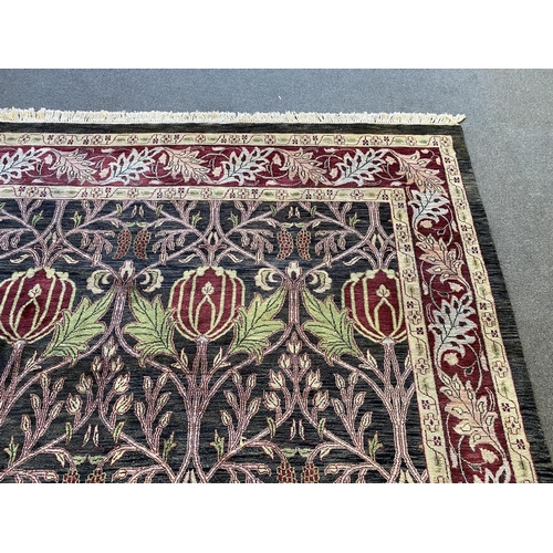 224 - A large Indian Arts & Crafts style carpet, with stylised pomegranate and flower motifs on a charcoal... 