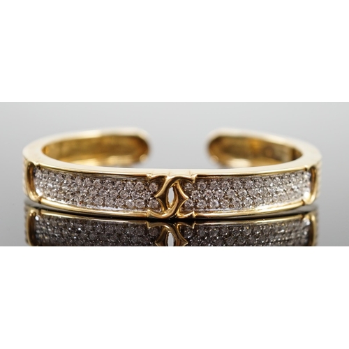 649 - A modern 18k gold and pave set diamond Cartier open work hinged bangle, with central crossed C's mot... 