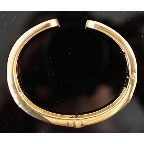 649 - A modern 18k gold and pave set diamond Cartier open work hinged bangle, with central crossed C's mot... 