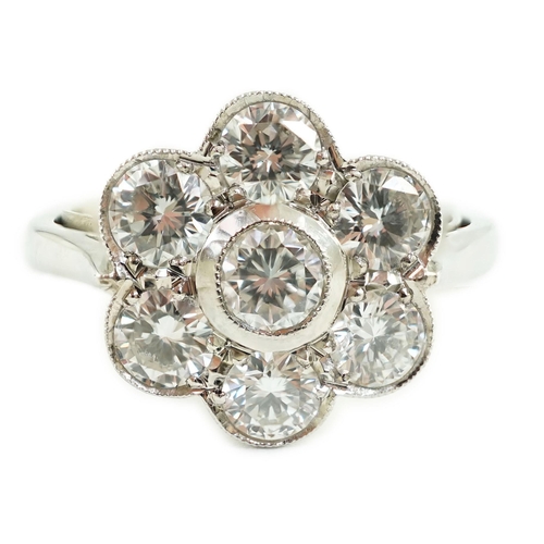 653 - A platinum and seven stone diamond cluster set flower head ring, the millegrain set stones with an a... 