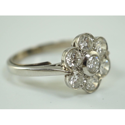 653 - A platinum and seven stone diamond cluster set flower head ring, the millegrain set stones with an a... 