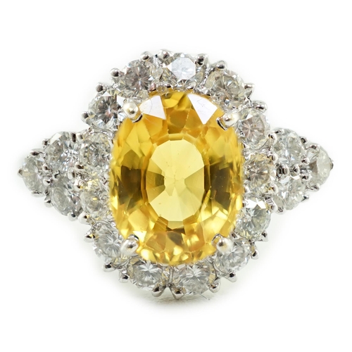 662 - A modern 18ct white gold and single oval cut yellow sapphire set ring, bordered by round cut diamond... 