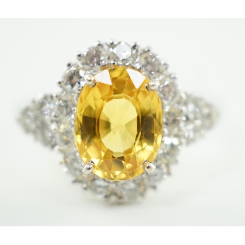 662 - A modern 18ct white gold and single oval cut yellow sapphire set ring, bordered by round cut diamond... 