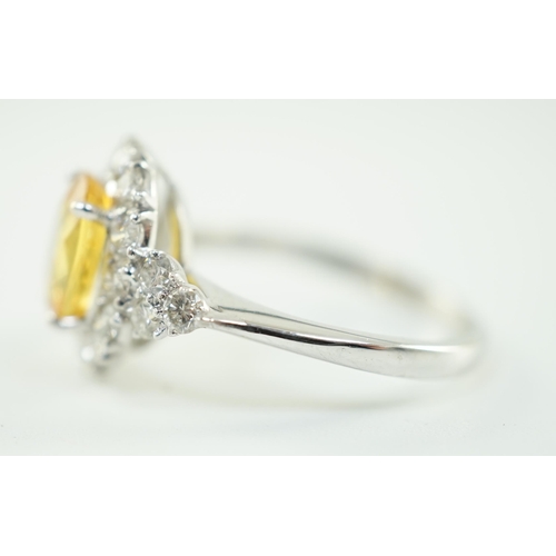 662 - A modern 18ct white gold and single oval cut yellow sapphire set ring, bordered by round cut diamond... 