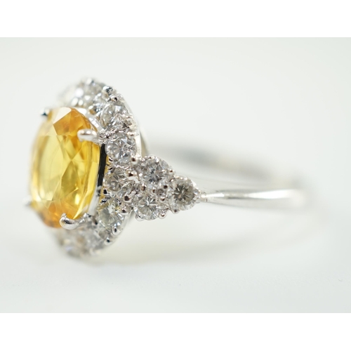 662 - A modern 18ct white gold and single oval cut yellow sapphire set ring, bordered by round cut diamond... 