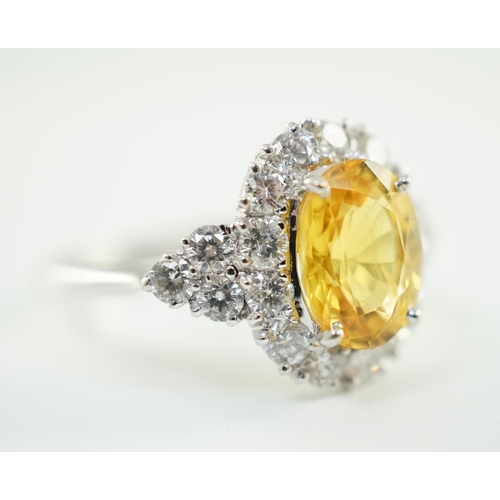 662 - A modern 18ct white gold and single oval cut yellow sapphire set ring, bordered by round cut diamond... 