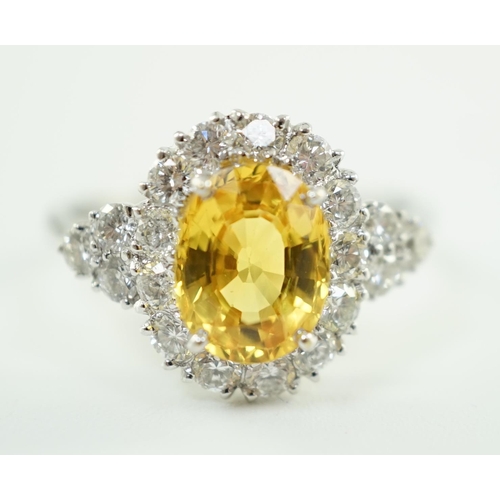 662 - A modern 18ct white gold and single oval cut yellow sapphire set ring, bordered by round cut diamond... 