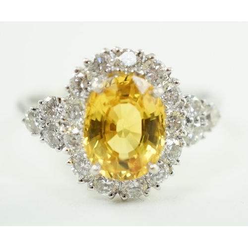 662 - A modern 18ct white gold and single oval cut yellow sapphire set ring, bordered by round cut diamond... 