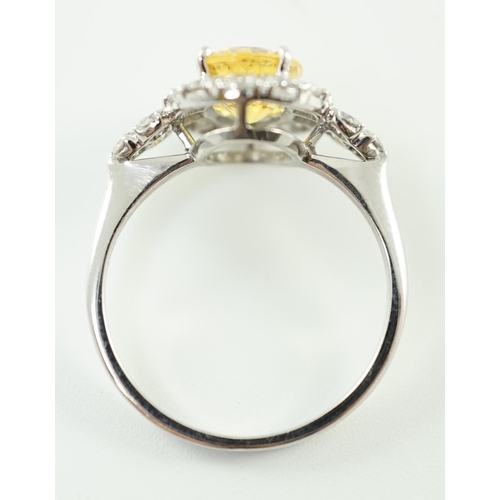 662 - A modern 18ct white gold and single oval cut yellow sapphire set ring, bordered by round cut diamond... 