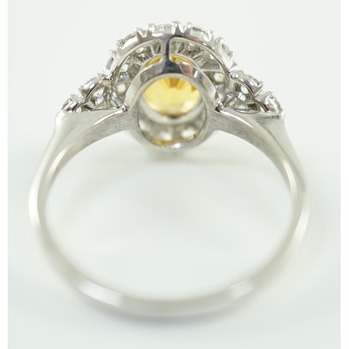 662 - A modern 18ct white gold and single oval cut yellow sapphire set ring, bordered by round cut diamond... 