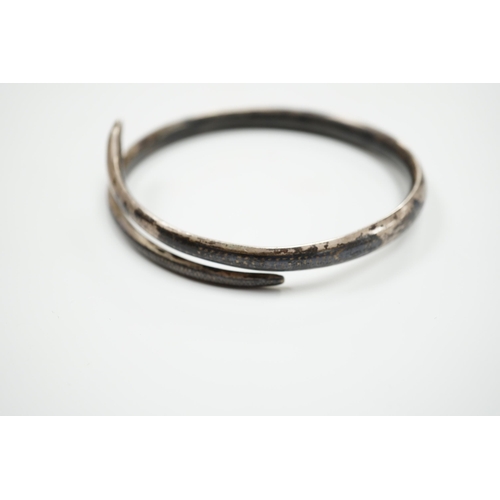 939 - A white metal and niello serpent bangle, decorated with scene of a camel train.