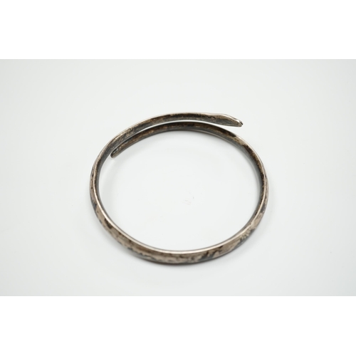 939 - A white metal and niello serpent bangle, decorated with scene of a camel train.