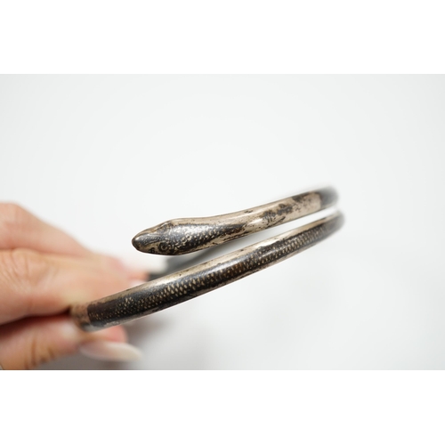 939 - A white metal and niello serpent bangle, decorated with scene of a camel train.