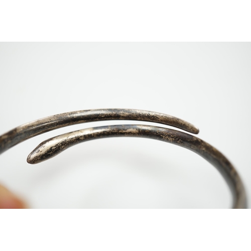 939 - A white metal and niello serpent bangle, decorated with scene of a camel train.