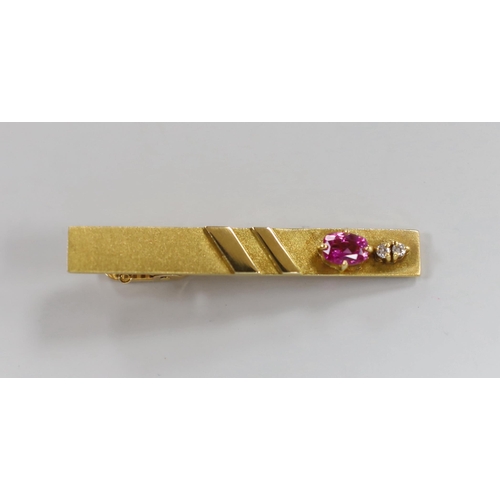 945 - A modern 18k, ruby and diamond set three stone tie clip, 47mm, gross weight 7.7 grams.